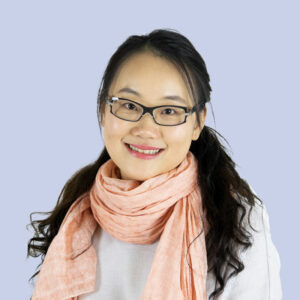 Smiling woman wearing glasses and a light pink scarf against a soft blue background, representing a friendly and approachable professional image.