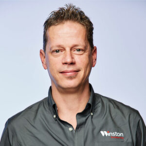Professional man in a gray shirt with the logo of Weston, posing against a neutral background.