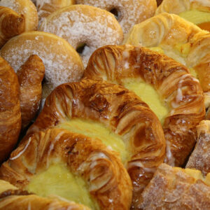Assorted fresh pastries including danishes, croissants, and powdered sugar-coated treats, showcasing a variety of textures and flavors.